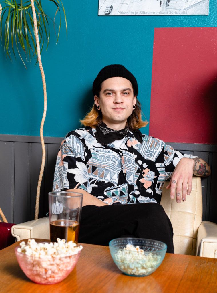 Willamo katsoo hymyillen kameraan, pöydällä popcorneja ja olutlasi.